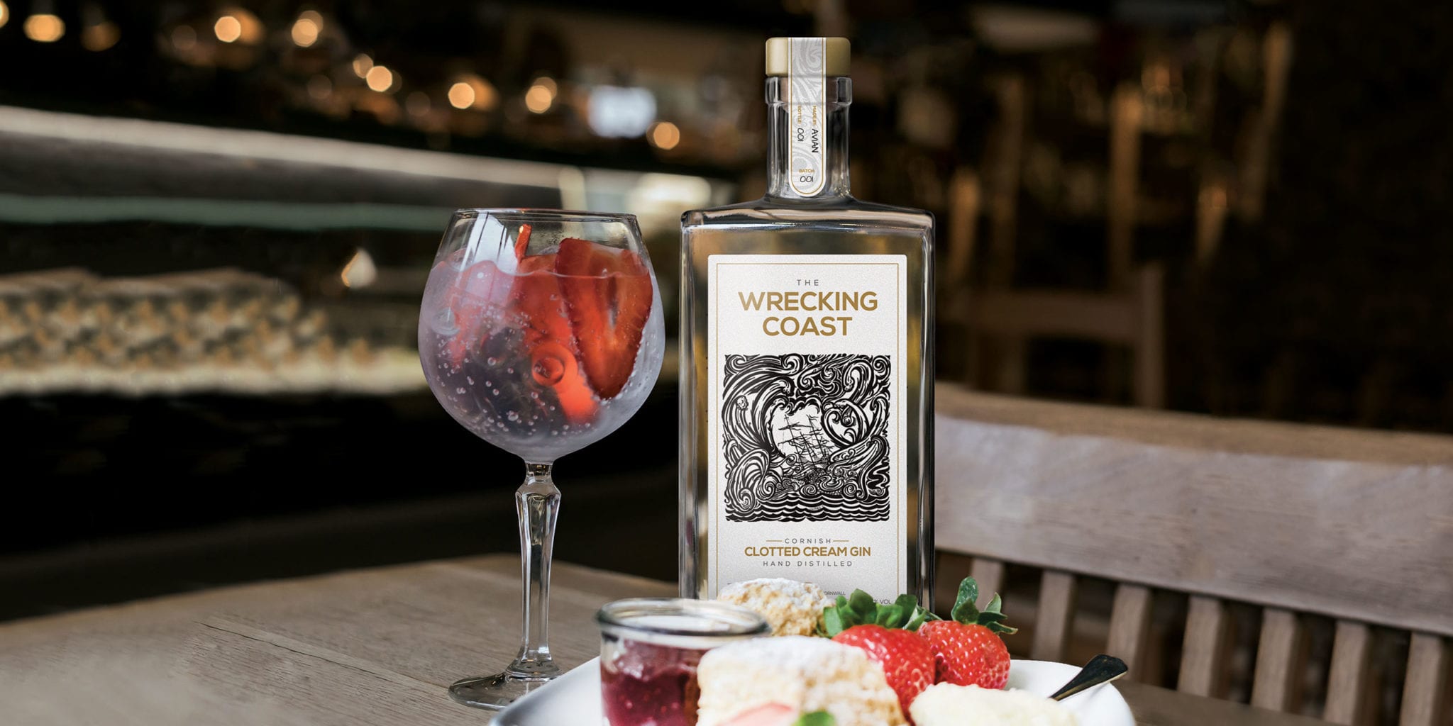 A Cornish Clotted Cream Gin bottle next to a glass of gin with strawberries and plated ingredients of a traditional Cornish cream tea