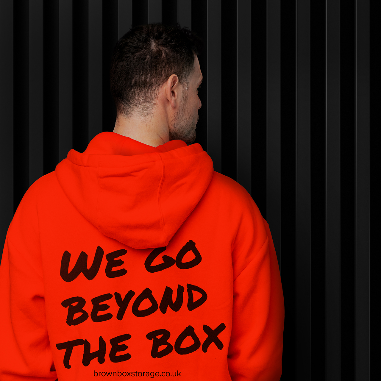Brown Box Self Storage Branded hoodie A gentleman with his back to the camera wearing a Brown Box Self Storage Branded hoodie in orange with black text on it.